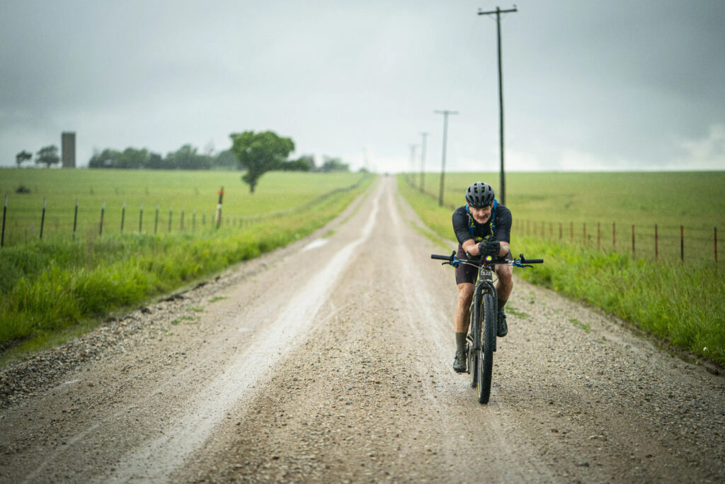Scenes from the course during the Unbound XL 2022: Dylan Morton rides in an aero position down a wide and wet gravel road. 