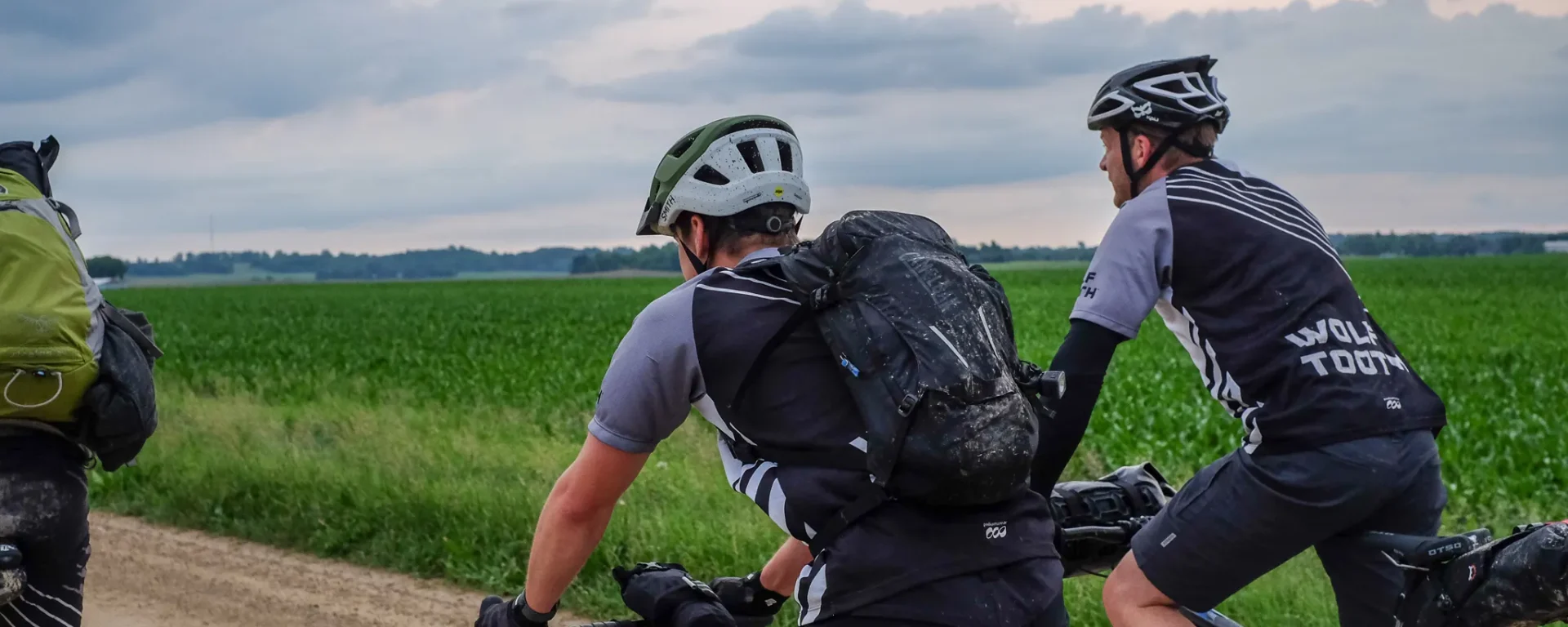 A group of cyclists riding their bikes. They are on a bikepacking trip in Minnesota. It has recently rained, so the landscape (and cyclists) appear to be damp.